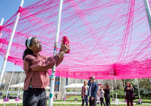 Student creating an art installation with pink yarn on UNC Asheville's Quad
